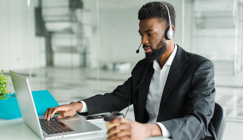 African american man customer support operator with hands-free headset working in the office. African american customer support operator with hands-free headset working in the office.